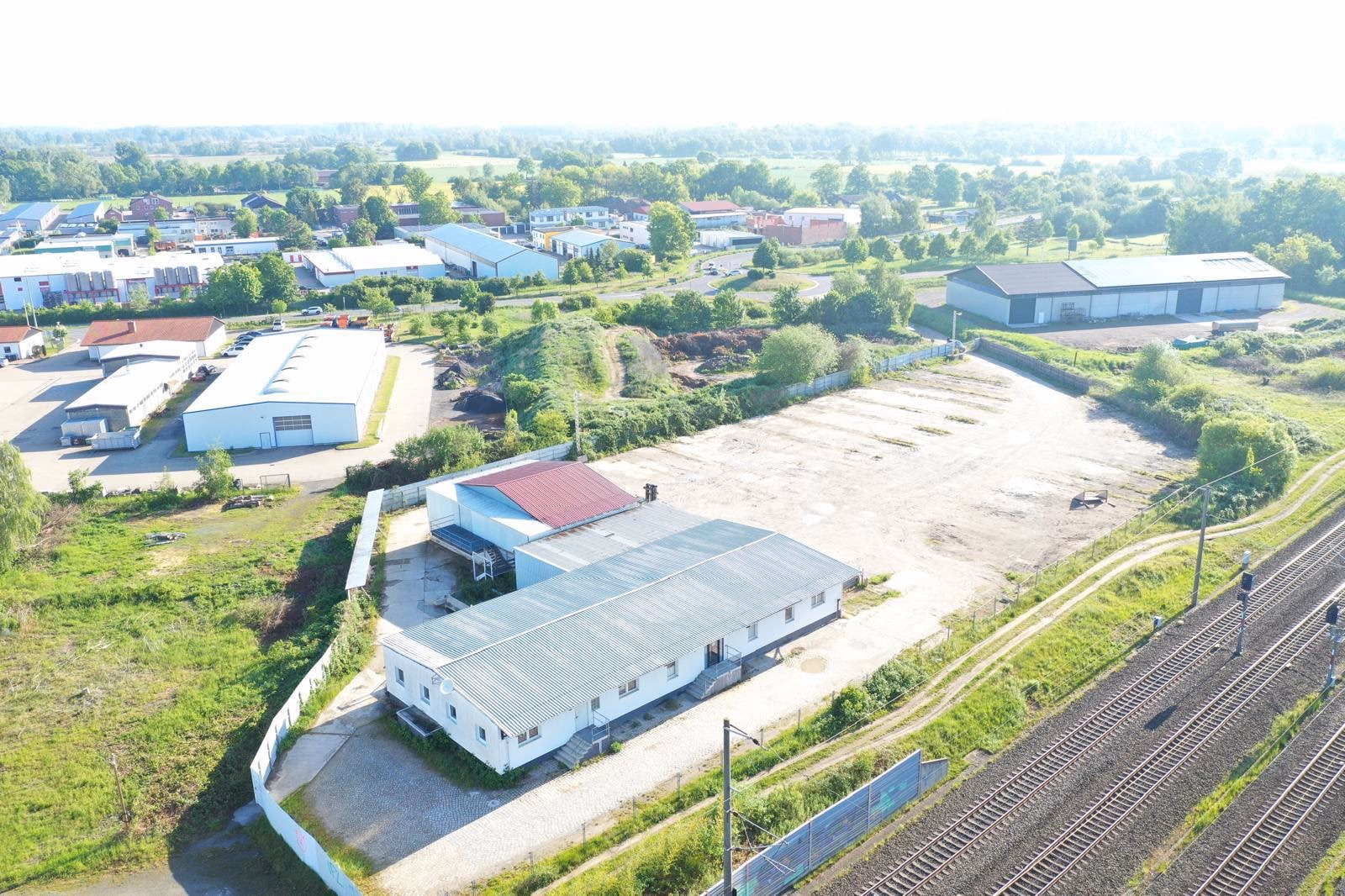 Drohnenaufnahme von Bürogebäude und Freifläche entlang der Bahnstrecke